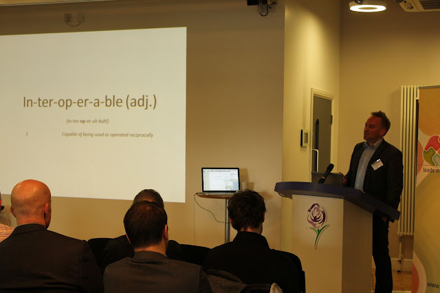 fotografía de una presentación con un señor en un atril y una diapositiva con la palabra "interoperable"